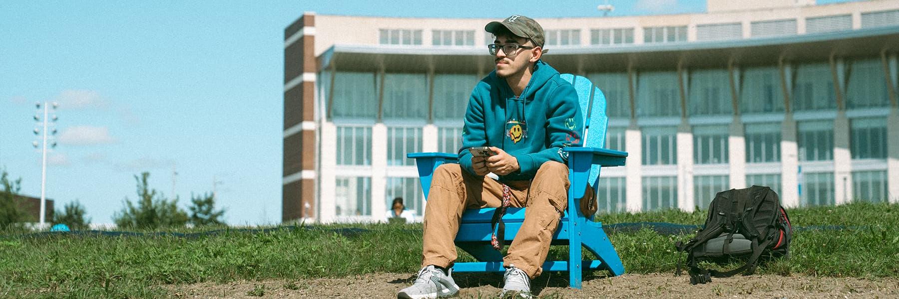 学生坐在校园中心草坪上的蓝色椅子上，手里拿着手机.